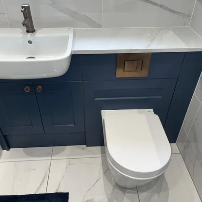 Bathroom with navy shaker vanity, white semi-recessed sink, brushed bronze fixtures, wall-hung toilet, and white marble-effect wall and floor tiles.