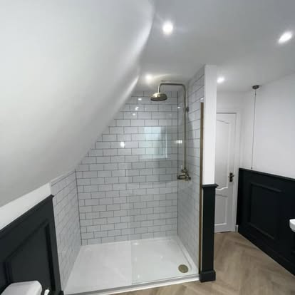 Attic bathroom walk-in shower with white subway tiles, gold rain shower and mixer, herringbone wood floor, and dark wainscoting under a sloped ceiling.