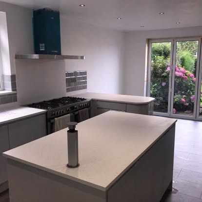 Bright renovated kitchen with white island, grey subway backsplash, black range cooker with hood still in protective plastic, and patio doors to the garden.