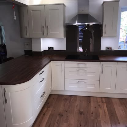 Transitional kitchen with pale shaker cabinets, dark wood-effect countertops and flooring, induction hob, and stainless chimney extractor.